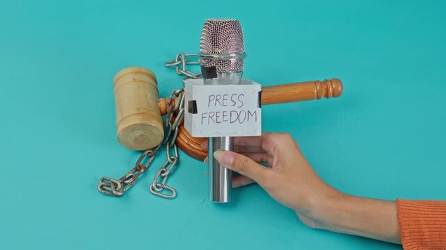 Hand Places Microphone Labeled "Press Freedom" Next To Wooden Judge'S Gavel Bound In Metal Chains For Intersection Of Law And Media Rights