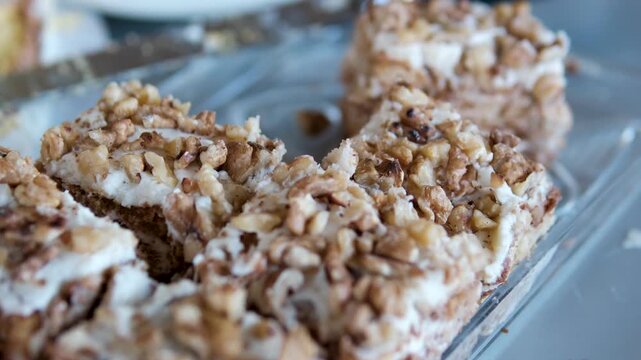 Slices of honey cake are arranged on a rectangular glass plate and sprinkled with nuts. The dessert is presented on a buffet table, highlighting a rich layered texture and festive serving style. 