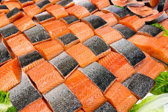 Neatly arranged fresh salmon fillets with skin on display at a fish market.