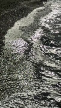 Slow-motion vertical 4K footage of ocean waves gently but powerfully rolling onto a sandy beach on a windy day