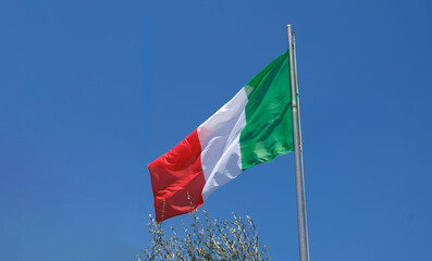 Italian flag waving on a pole against a clear blue sky. Democracy and politics. European country. For travel, culture, patriotism