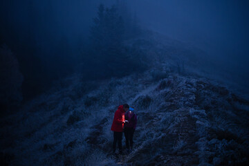 Obraz premium Couple Hiking at Night on a Foggy Mountain Ridge Using Phone and Headlamp for Navigation