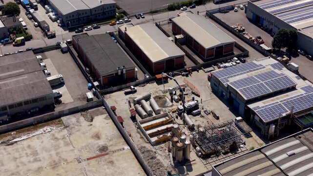 Aerial drone view of a chemical plant under construction in an industrial zone of Milan, Italy. Large structures, cranes and infrastructure show active development of heavy industry.