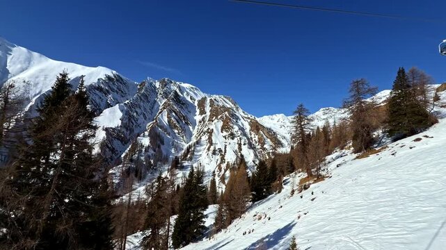 A chairlift glides over snow-covered slopes in an alpine region, framed by rugged mountains and clear blue skies. Ideal for winter sports or travel-themed projects.