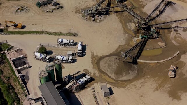 Aerial drone view of concrete plant at gravel quarry. Mixer trucks line up in queue to load fresh concrete in an active industrial production site.