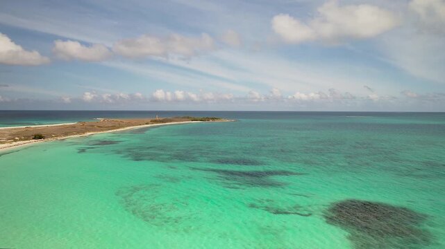 drone shot tilt down over iconic Cayo de Agua island in Los Roques, surrounded by pristine turquoise Caribbean waters and lighthouse in background