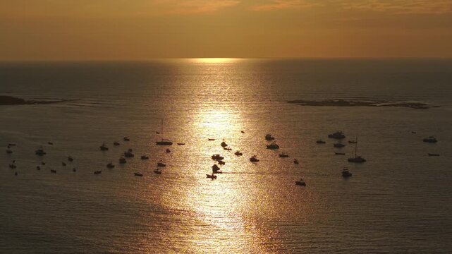 Aerial zoom out revealing Tamarindo bay filled with boats under warm sunset reflection on ocean.