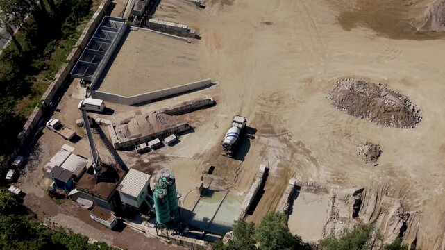 Gravel quarry with industrial concrete plant. Multiple mixer trucks waiting in queue for loading within large construction materials production site.