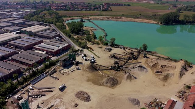 Gravel quarry in Italy with concrete plant and industrial production lines. Heavy machinery operates in large-scale construction materials site.