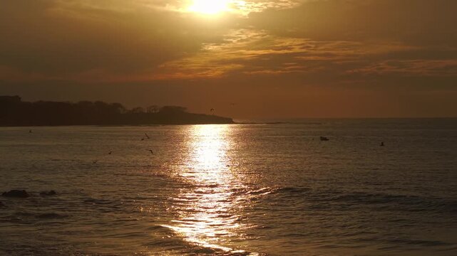 Aerial pan right capturing Tamarindo coastline with glowing sunset and calm ocean surface.