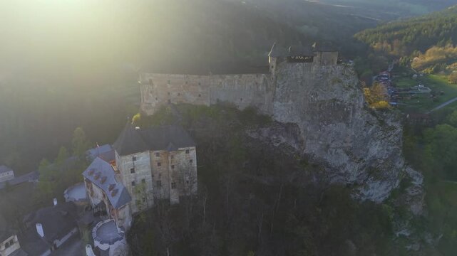 Aerial view flying over the historic Orava Castle in Slovakia. Beautiful medieval landmark perched on a rocky cliff above a river at sunset