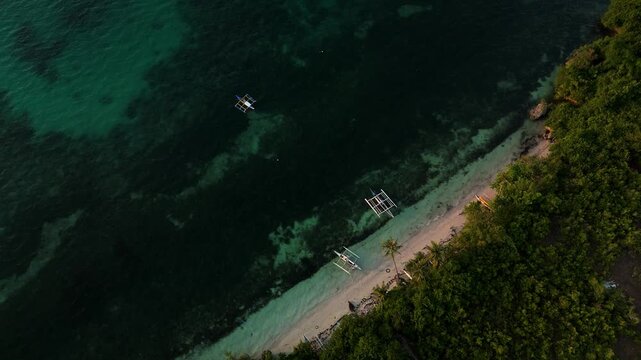 Drone descends over a top-down sunset view of Panglao Island beach, boats, reef flats, and shoreline in Bohol