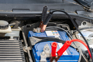 Fototapeta premium a blue car battery inside an engine compartment with black and red jumper cables clamped to its terminals for a jump-start.