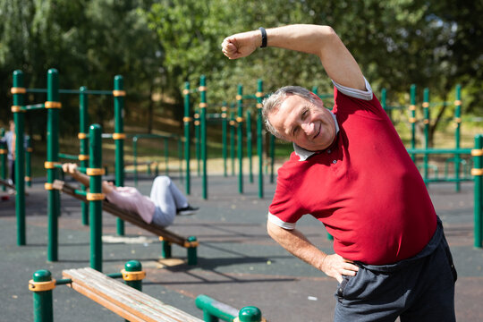 elderly man does gymnastics on an outdoor sports ground.