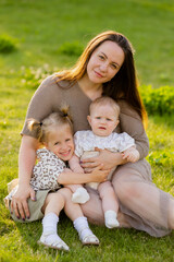 Fototapeta premium mother with two daughters sitting on a lawn at sunset in the summer, hugging