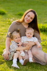 Fototapeta premium mother with two daughters sitting on a lawn at sunset in the summer, hugging