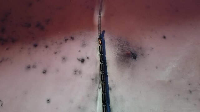 Aerial follow shot of train carrying salt through pink lake in Altai region