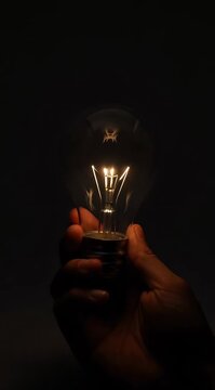 Close Up Of Hand Holding Lit Incandescent Light Bulb Against Dark Background Dramatic Lighting