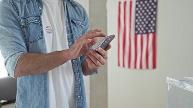 Man tapping smartphone with hands by ballot box and 'i voted' sticker in polling building; civic pride.