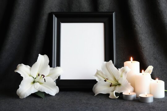Mockup with white lilies and lit candles next to black frame on dark fabric. Suitable for memorial tribute sympathy condolence cards funeral announcements.