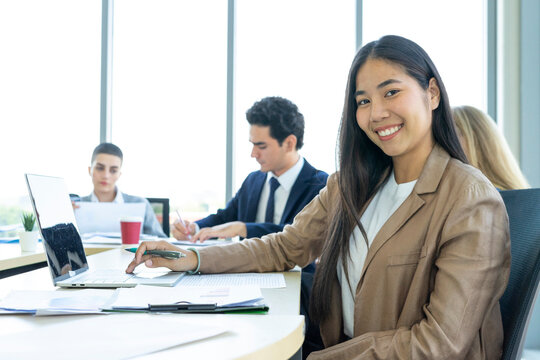 Young cheerful Asian business woman discussing project with colleagues while working together in the modern office.