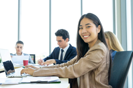 Young cheerful Asian business woman discussing project with colleagues while working together in the modern office.