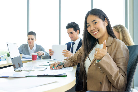 Young cheerful Asian business woman discussing project with colleagues while working together in the modern office.