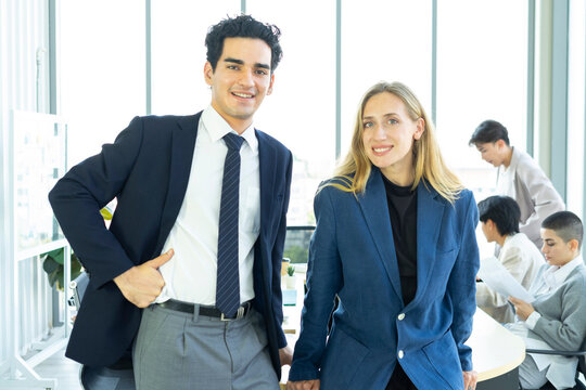Businesswoman and businessman leader looking at camera in modern office with businesspeople working at the background. Teamwork concept. 
