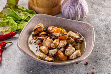 Fototapeta premium Marinated mussels in a ceramic bowl with chili and garlic on a concrete table.
