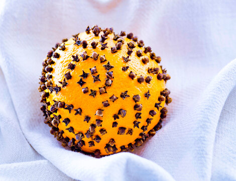 Aromatic orange pomander with cloves on white fabric