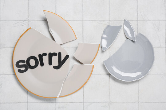 Broken plates with word SORRY on white tiled table