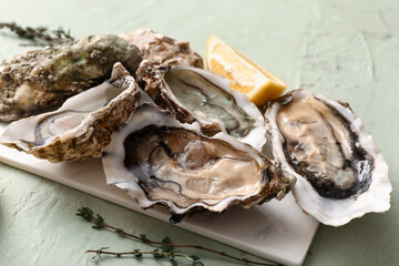 Board with delicious fresh oysters, thyme and lemon on green background, closeup © Pixel-Shot