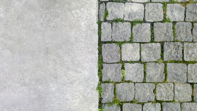 Contrasting textures of a paved road with rough concrete and uneven cobblestones featuring green moss and grass growing between the stone blocks