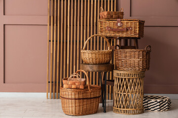 Fototapeta premium Different wicker baskets and wooden table near brown wall in stylish room
