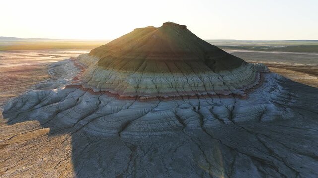 Aerial view of Mount Bokty featuring unique colorful sedimentary layers and eroded slopes under golden sunlight in the desert of Karakiya District, Mangystau Region, Kazakhstan.