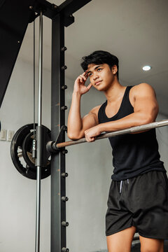 Focused young athlete rests on a smith machine while reflecting after an intense gym workout and strength training session