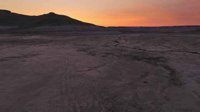 Aerial view of Gora Bokty with silhouetted mountain peaks and vast desert plains under a vibrant sunset sky in Karakiya District, Mangystau Region, Kazakhstan.