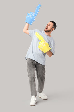 Happy young man with foam fingers pointing at something on grey background. Sports bet concept