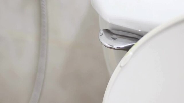 person hand lift the flapper to release water tank flush lever handle bathroom Flush the toilet close-up. Slow motion 4K Flushing water in toilet UHD