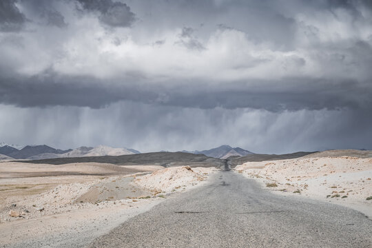 The Pamir Highway in the Tien Shan highlands of the Pamirs in Tajikistan, an asphalt road stretching into the distance, desert terrain with mountains