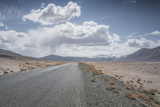 The Pamir Highway in the Tien Shan highlands of the Pamirs in Tajikistan, an asphalt road stretching into the distance, desert terrain with mountains