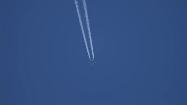 Overhead airplane centered in frame leaving twin contrails upward in clear blue sky, vertical flight perspective and minimal composition. Parallel vapor trails emphasizing altitude, speed and jet