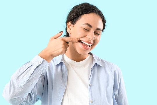Young African-American woman showing her teeth on blue background, closeup
