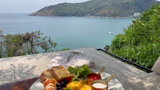 Elegant tropical breakfast served overlooking the Andaman Sea in Phuket, featuring fresh bread, smoked salmon, avocado, shrimp, salad, sauces, and panoramic coastal scenery in a luxury vacation spot