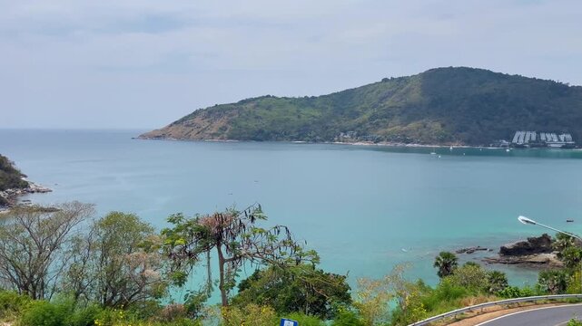 Scenic panoramic view of Nai Harn Beach in Phuket with turquoise water, green tropical hills, coastal road, and peaceful seaside atmosphere on a sunny day in southern Thailand