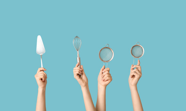 Female hands holding sieves with cake spatula and whisk on blue background