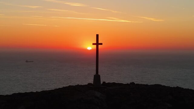 The sun rises over the ocean, silhouetting a cross on a hilltop in Bray. Ideal for spiritual themes or travel content.