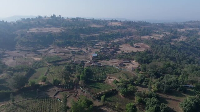 Remote village settlement in Vansda, Gujarat, India, showing scattered houses and agricultural plots across hilly terrain. Slow forward drone shot moving closer to the rural traditional houses.