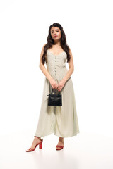 Naklejka premium Stylish young woman poses elegantly in a trendy summer dress on a bright studio backdrop