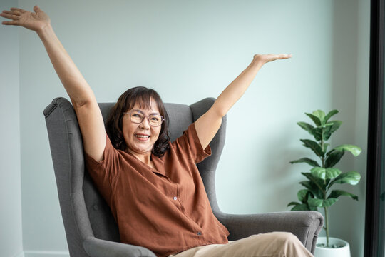 Happy senior woman wearing eyeglasses enjoy relaxing and looking at camera while sitting on sofa at home, happiness retirement and mental health wellbeing lifestyle concept.